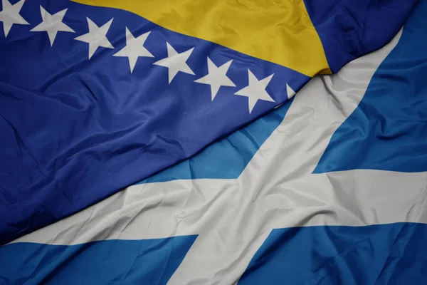 waving colorful flag of scotland and national flag of bosnia and herzegovina.