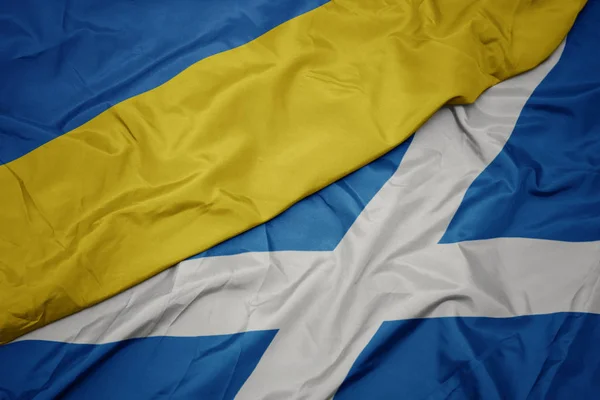 waving colorful flag of scotland and national flag of ukraine.