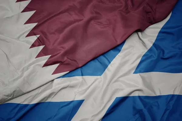 waving colorful flag of scotland and national flag of qatar.