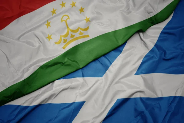 waving colorful flag of scotland and national flag of tajikistan.