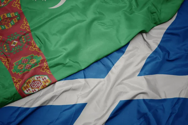 waving colorful flag of scotland and national flag of turkmenistan.