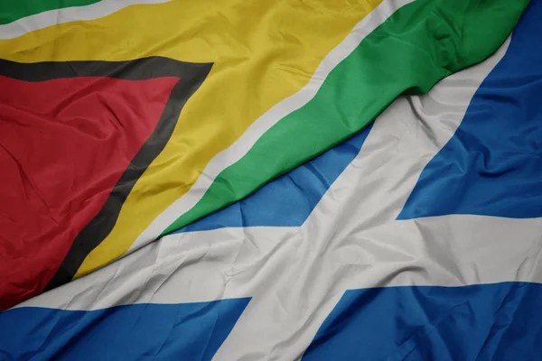 waving colorful flag of scotland and national flag of guyana.