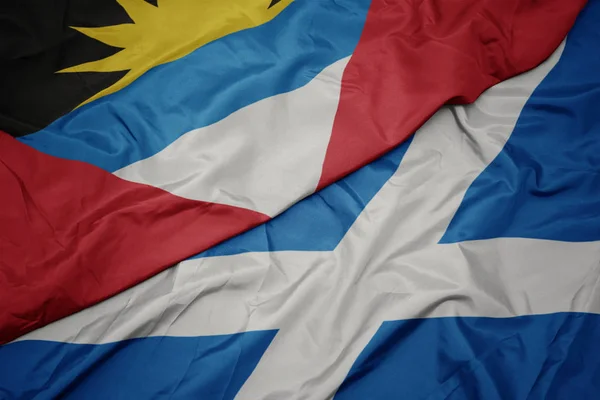 waving colorful flag of scotland and national flag of antigua and barbuda.