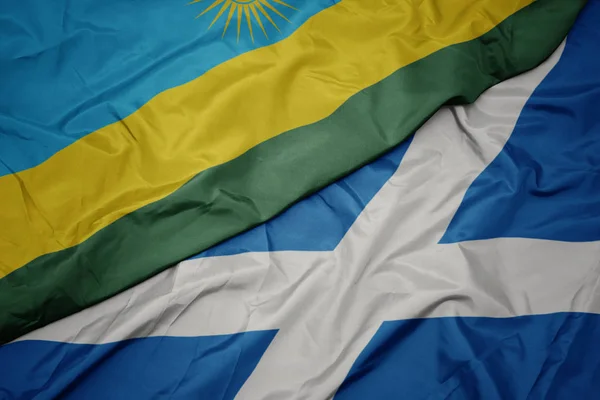Acenando bandeira colorida da Escócia e bandeira nacional do Ruanda . — Fotografia de Stock