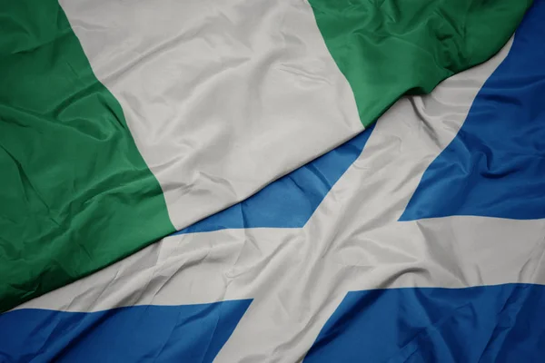 waving colorful flag of scotland and national flag of nigeria.