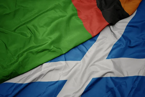 waving colorful flag of scotland and national flag of zambia.