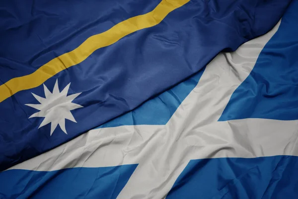 waving colorful flag of scotland and national flag of Nauru .