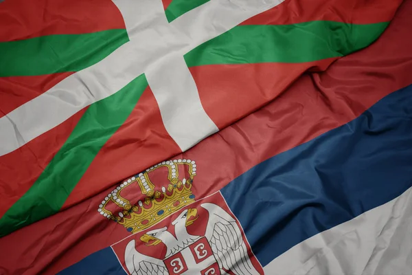 waving colorful flag of serbia and national flag of basque country.