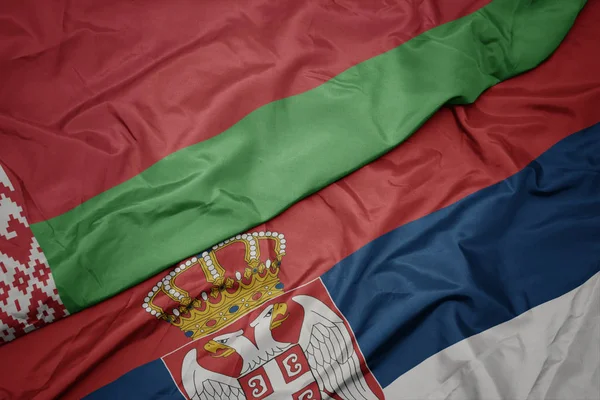 waving colorful flag of serbia and national flag of belarus.