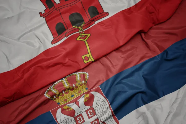 Agitant drapeau coloré de la serbie et drapeau national de gibraltar . — Photo