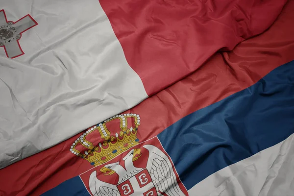waving colorful flag of serbia and national flag of malta.