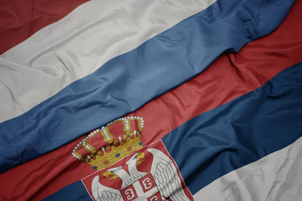 Agitant drapeau coloré de la serbie et drapeau national du luxembourg . — Photo