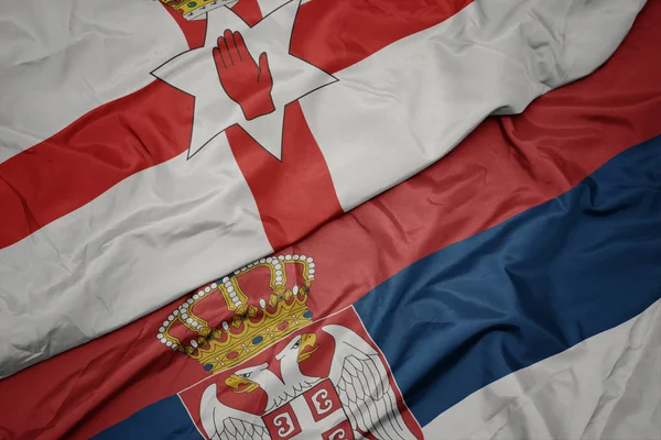 waving colorful flag of serbia and national flag of northern ireland.