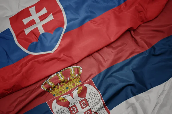 waving colorful flag of serbia and national flag of slovakia.