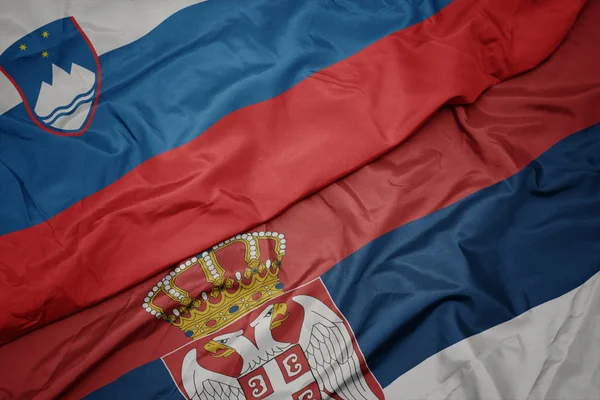 Ondeando colorida bandera de serbia y bandera nacional de slovenia . —  Fotos de Stock