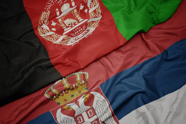 waving colorful flag of serbia and national flag of afghanistan.