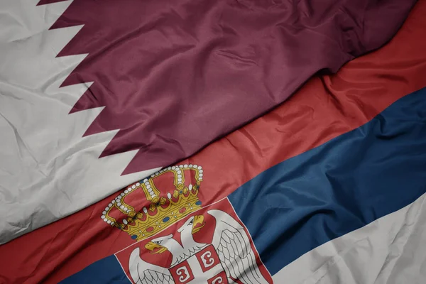 waving colorful flag of serbia and national flag of qatar.