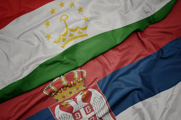 Agitant le drapeau coloré de la serbie et le drapeau national du tadjikistan . — Photo