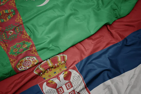 waving colorful flag of serbia and national flag of turkmenistan.