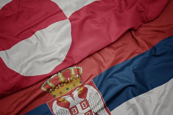 waving colorful flag of serbia and national flag of greenland.