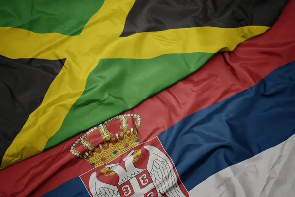 waving colorful flag of serbia and national flag of jamaica.