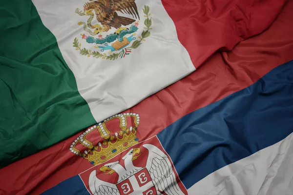 waving colorful flag of serbia and national flag of mexico.