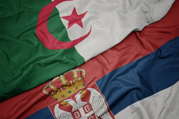 waving colorful flag of serbia and national flag of algeria