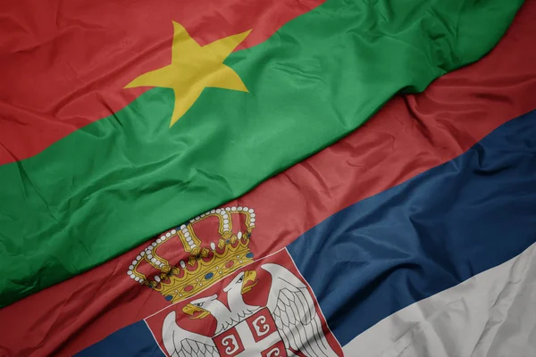 waving colorful flag of serbia and national flag of burkina faso.