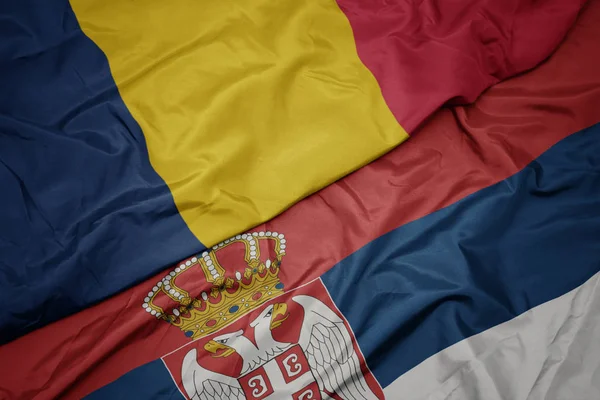 waving colorful flag of serbia and national flag of chad.