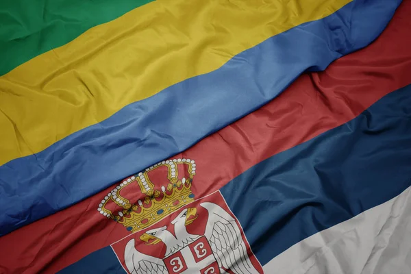 Acenando bandeira colorida da Sérvia e bandeira nacional do gabão . — Fotografia de Stock