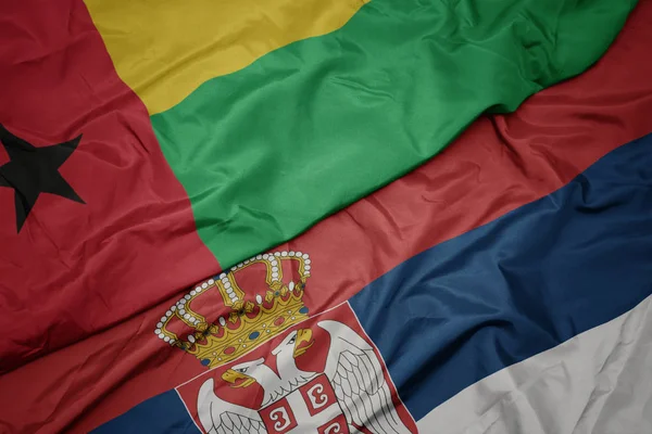 waving colorful flag of serbia and national flag of guinea bissau.