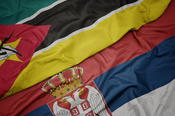 waving colorful flag of serbia and national flag of mozambique.