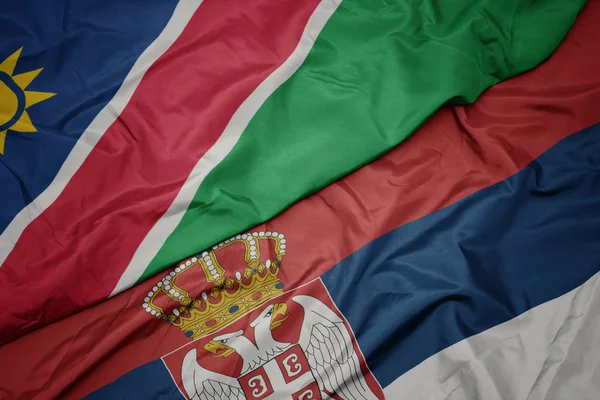 waving colorful flag of serbia and national flag of namibia.