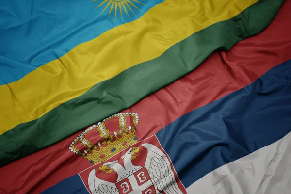 waving colorful flag of serbia and national flag of rwanda.