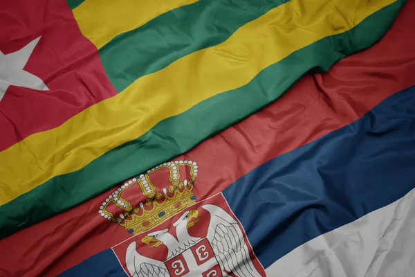 waving colorful flag of serbia and national flag of togo.