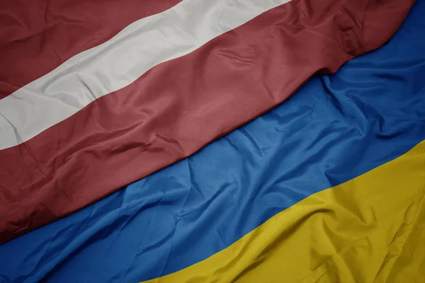 Waving colorful flag of ukraine and national flag of latvia. — Stock Photo, Image