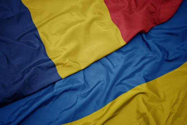 Agitant drapeau coloré de l'ukraine et drapeau national de la Roumanie . — Photo