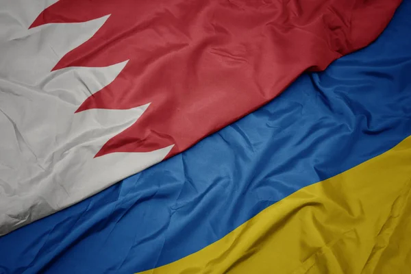 waving colorful flag of ukraine and national flag of bahrain.