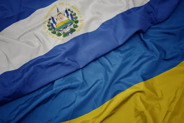 Ondeando colorida bandera de Ucrania y bandera nacional del salvador . — Foto de Stock