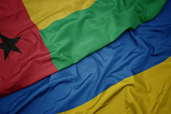 Sventolando bandiera colorata dell'Ucraina e bandiera nazionale della Guinea bissau . — Foto Stock