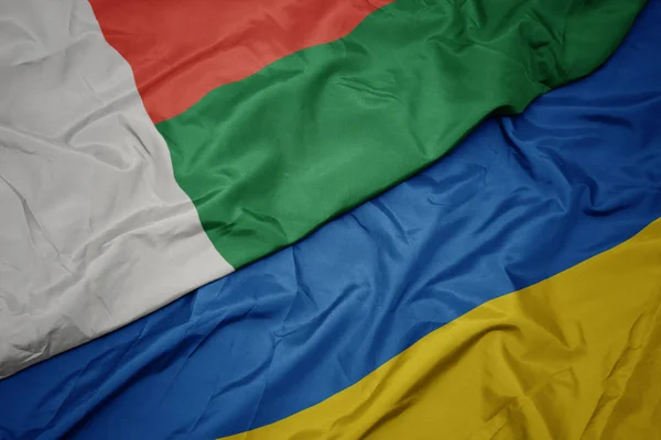 Schwenken bunte Fahne der Ukraine und Nationalflagge Madagaskars. — Stockfoto