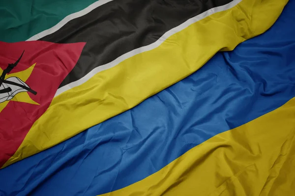 Acenando bandeira colorida de ucraniano e bandeira nacional de moçambique . — Fotografia de Stock