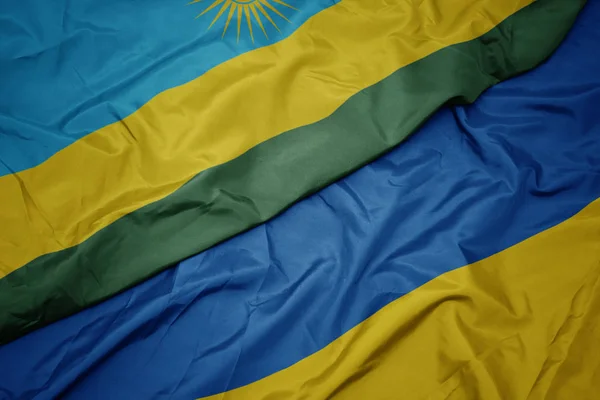 Waving colorful flag of ukraine and national flag of rwanda. — Stock Photo, Image