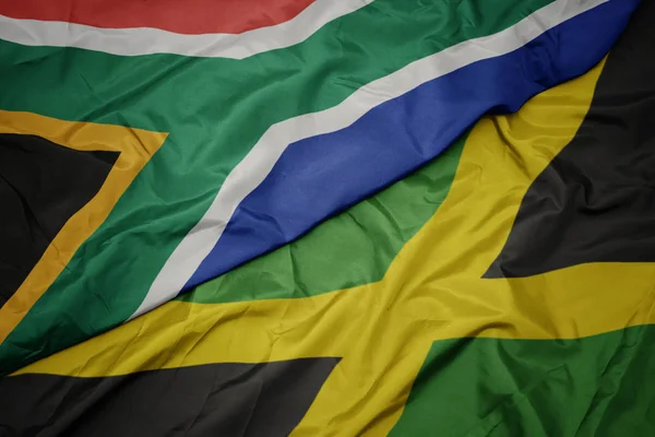 Agitant drapeau coloré de la Jamaïque et drapeau national de l'Afrique du Sud . — Photo