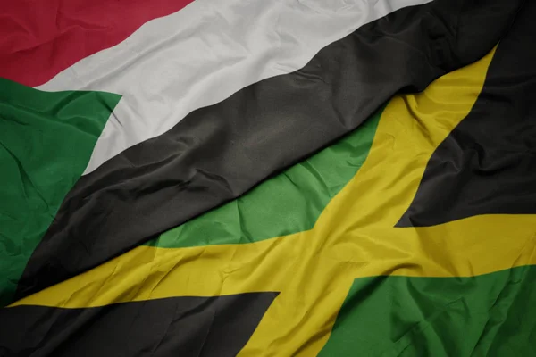 Ondeando colorida bandera de jamaica y bandera nacional de sudan . — Foto de Stock