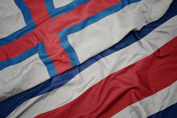 Ondeando colorida bandera de costa rica y bandera nacional de las islas Feroe . — Foto de Stock