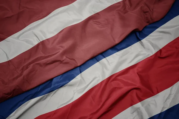 Ondeando colorida bandera de costa rica y bandera nacional de latvia . — Foto de Stock