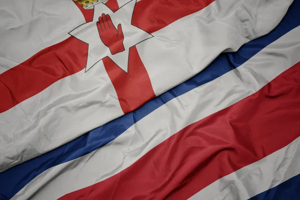 Zwaaiende vlag van Costa Rica en nationale vlag van Noord-Ierland. — Stockfoto