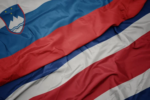 Schwenken bunte Flagge Costa Ricas und slowenische Nationalflagge. — Stockfoto