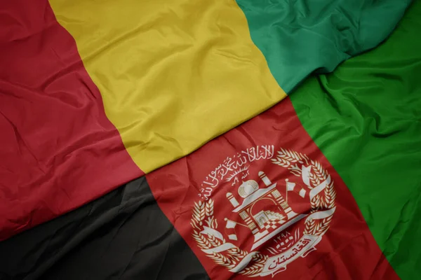 waving colorful flag of afghanistan and national flag of guinea.